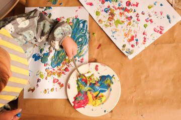 A child’s hand painting with bright finger paints at table covered with brown paper. Shot directly above - Powered by Adobe