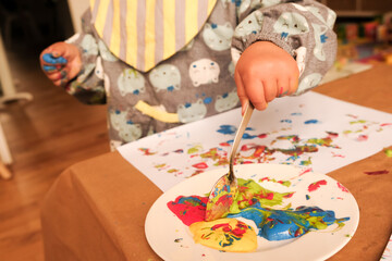 Obraz premium A child’s hand painting with bright finger paints at table covered with brown paper. 