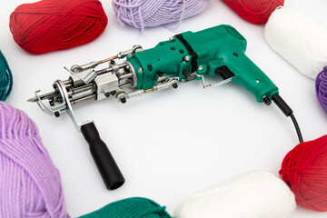 Tufting gun and skeins of yarn of various colors on white background. Cut and pile gun. Carpet hand tufting machine