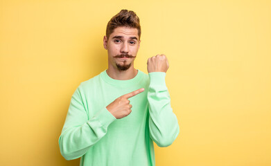 young handsome man looking impatient and angry, pointing at watch, asking for punctuality, wants to...