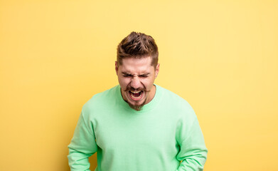young handsome man shouting aggressively, looking very angry, frustrated, outraged or annoyed,...