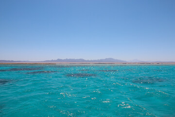 Obraz premium Seascape. Clear azure water with coral reefs and a desert mountain range on the horizons. Clear sunny sky