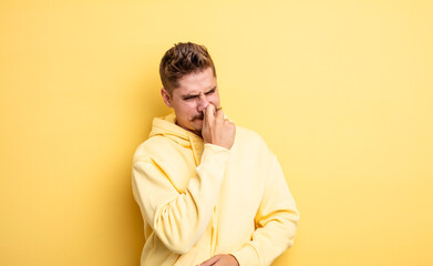 young handsome man feeling disgusted, holding nose to avoid smelling a foul and unpleasant stench....