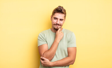 young handsome man smiling with a happy, confident expression with hand on chin, wondering and...