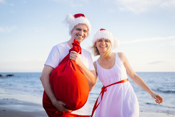 Obraz premium Happy family in Santa Claus hats celebrating Christmas on beach. Smiling people traveling to warm countries on winter tour. New Year and Christmas tourists