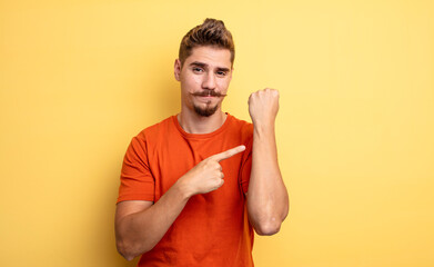 young handsome man looking impatient and angry, pointing at watch, asking for punctuality, wants to...