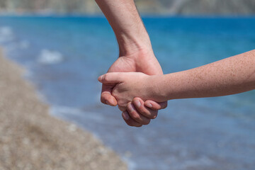 Couple hands held together on a natural sea background, close up