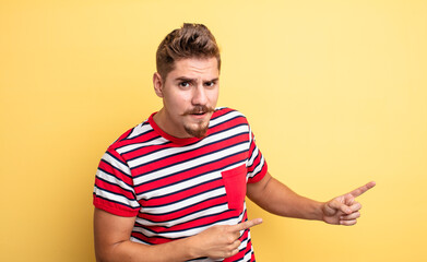 young handsome man feeling shocked and surprised, pointing to copy space on the side with amazed,...