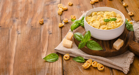 Tortellini soup, brodo on a wooden board with basil and parmesan. Cuisine from Bologna and Emilia Romagna: Cappelletti, fresh egg pasta with meat and vegetables filling. Copy space. Banner