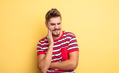 young handsome man holding cheek and suffering painful toothache, feeling ill, miserable and...