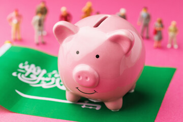 Piggy bank, the flag of Saudi Arabia and plastic toy men on a colored background, the concept on the theme of the income of the population of Saudi Arabia
