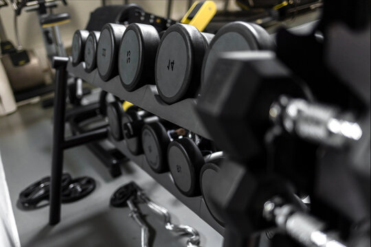 Rows of dumbbells in the gym with sunlight in morning. Sports dumbbells in modern sports club. Weight training equipment. Dumbbell set in sport fitness center room for healthy background concept