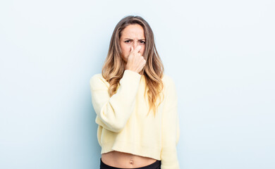 pretty caucasian woman feeling disgusted, holding nose to avoid smelling a foul and unpleasant...