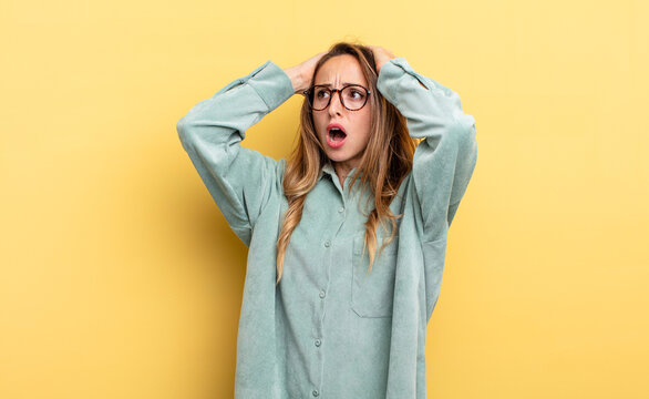 pretty caucasian woman with open mouth, looking horrified and shocked because of a terrible mistake, raising hands to head