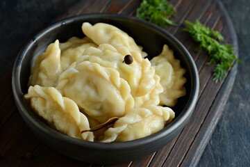 Dumplings (vareniki, pierogi, pyrohy) with potatoes, herbs, spices and butterin a ceramic bowl on a dark background. 