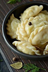 Dumplings (vareniki, pierogi, pyrohy) with potatoes, herbs, spices and butterin a ceramic bowl on a dark background. 