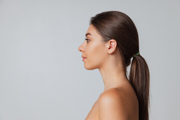 Side view. Young adorable naked girl looking at camera isolated over gray studio background. Natural beauty concept.