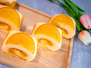 Close up of orange cake roll with slice orange fruit on wooden plate.