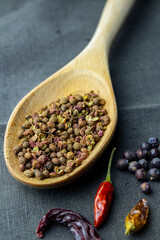 sichuan paper in wood spoon, chilli paper and juniper berry on dark gray cloth