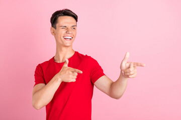 Photo of impressed flirty young man wear red t-shirt smiling winking pointing fingers empty space...
