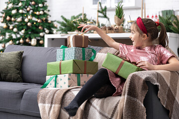 Obraz premium A little girl enjoys a lot of Christmas gifts sitting on the couch at home.