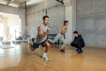 Fototapeta na wymiar Fitness trainer trains man and woman to do lunge exercise in a gym.
