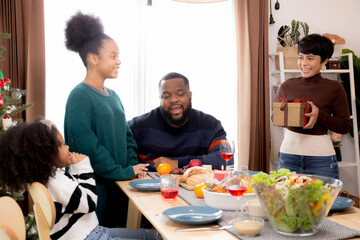 Happy family with mother giving gift box with daughter during dinner at home, celebration in xmas with parent surprising children with enjoyment at house, thanksgiving eve, Merry Christmas.