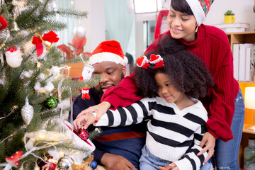 Happy family with father and mother decorating ornament on Christmas tree with daughter together at home, thanksgiving eve, celebration of bonding in Christmas day, enjoyment and fun on holiday.