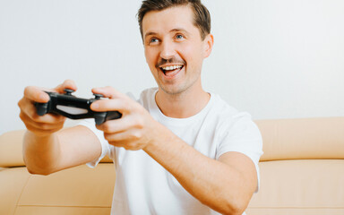 Happy young man playing video game with joystick, enjoying active leisure while sitting on sofa at home. Joyful guy player gamer with gamepad and hobby electronic sport