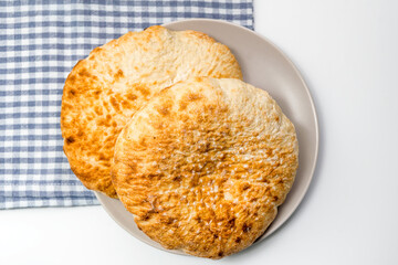 Loafs of flat round wheat bread in a plate, on a blue kitchen cloth over white table
