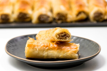 Meat rolls pastry - fried minced pork meat in spring rolls in a black oval plate, isolated on white background with stacks of rolls. Selective focus