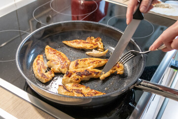 Woman cooking and frying chicken breasts and chicken filet in a pan on an hot stove in the kitchen as delicious meal and diet dinner cuisine for healthy nutrition with smoking hot meat and barbecue