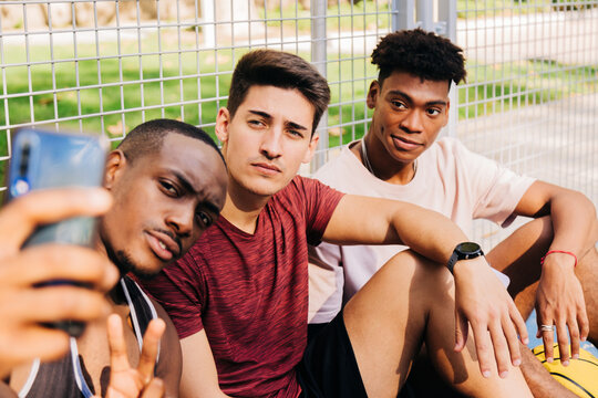 Cheerful diverse sportspeople taking selfie on smartphone in sports ground