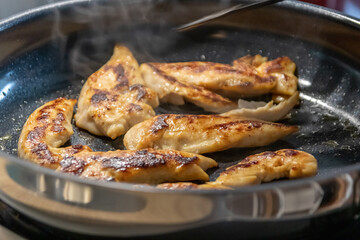 Woman cooking and frying chicken breasts and chicken filet in a pan on an hot stove in the kitchen as delicious meal and diet dinner cuisine for healthy nutrition with smoking hot meat and barbecue