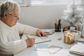 Healthy New Years resolutions for older adults. Senior mature old woman in white sweater writing handwritten text My Goals in open notepad on the table. Planning and setting goals - Powered by Adobe