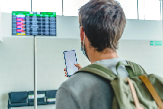 Crop traveler with phone near airport digital signage during pandemic