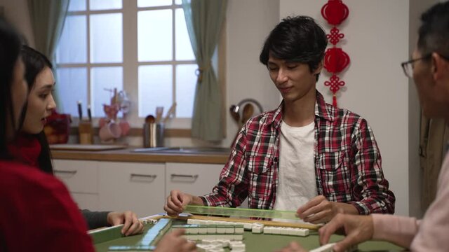 happy asian son in red plaid shirt saying ""wait"" with stop gesture and showing his hand, shouting ""mahjong"" as he completing set, clapping hands feeling proud of his win in tile game at home
