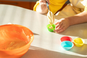 Girl in an apron prepares cupcakes in the kitchen. person preparing food in kitchen. 
