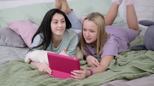Two teen girls sit at the laptop and look at the monitor chatting with friends over video chat.