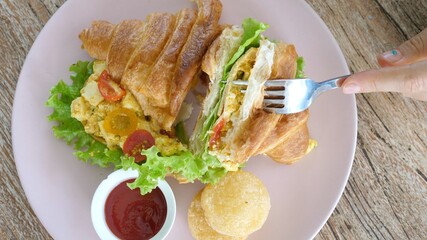 Top view of woman cutting croissant sandwich
