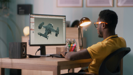 African American man in glasses using computer to create 3D model of aircraft while working at home office