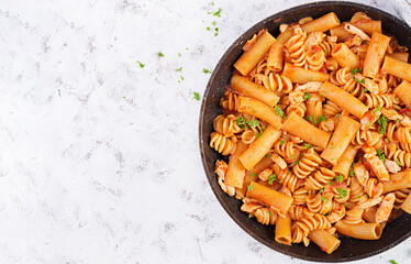 Fusilli pasta in tomato sauce with chicken, tomatoes decorated with parsley on light table. Top view