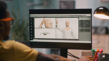 Black guy creating 3D model of bald human for movie or video game on computer during work in home...