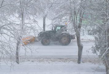 Tractor with snow plow plowing the road in heavy snow storm.