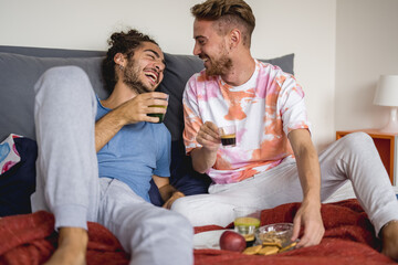 young gay couple in bed having breakfast, happy lovers drinking coffee and having fun in the...