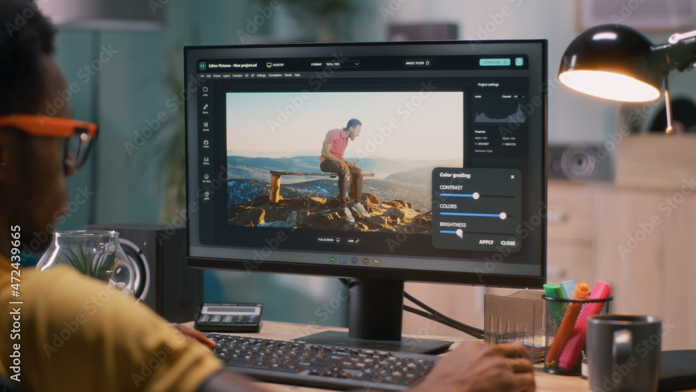 Poster black man adding 3d graphic into video with chromakey background while sitting at table and working 
