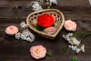 Chocolate flowers in a basket in the form of a heart. Roses, peonies on a brown wooden background.