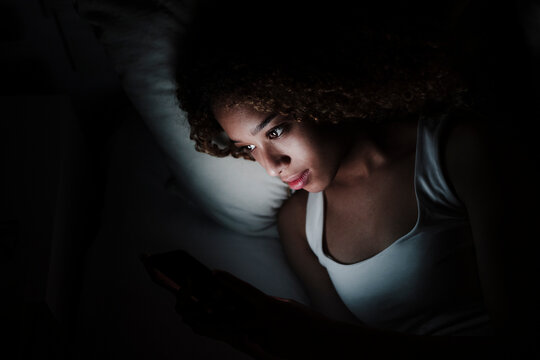 Woman using smart phone while lying on bed in dark room at home