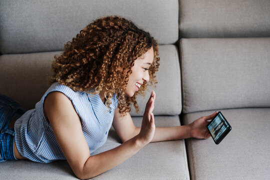 Smiling woman waving during video call through smart phone on sofa at home