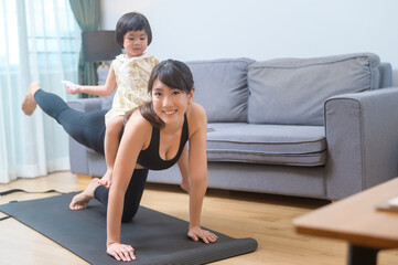 Fototapeta na wymiar Happy young woman in sportswear is with daughter exercising in living room at home